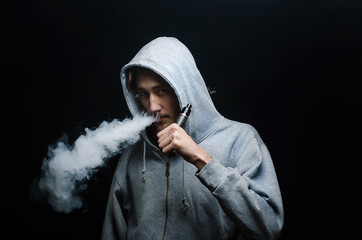 One man in the hood vaping e-cigarette and blowing a cloud.
