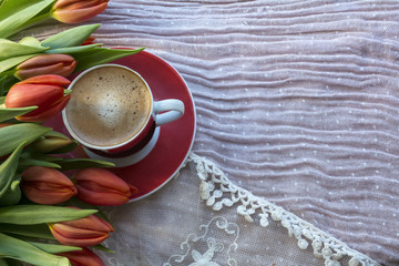 Red cup of black coffee with red tulips are on the light pink background