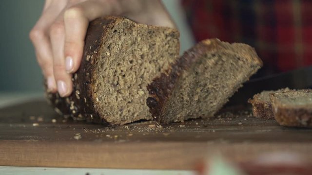 Close up of female hands slicing whole grain bread, super slow motion 240fps
