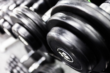Fototapeta na wymiar Rows of black dumbbells on a rack in a gym. Sports equipment for exercise, gymnastics, fitness, bodybuilding, training, sport, workout