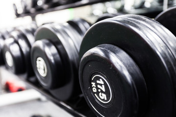 Fototapeta na wymiar Rows of black dumbbells on a rack in a gym. Sports equipment for exercise, gymnastics, fitness, bodybuilding, training, sport, workout