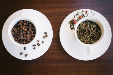 Cup  with  dried tea leaves and cup with coffee beans on wooden background. Common caffeinated drinks. Popular beverages concept. Top view.