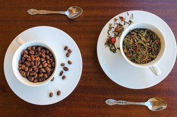 Cup  with  dried tea leaves and cup with coffee beans on wooden background. Common caffeinated drinks. Popular beverages concept. Top view.