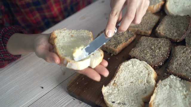 Close up of female hands spreading butter on bread in kitchen, super slow motion 240fps
