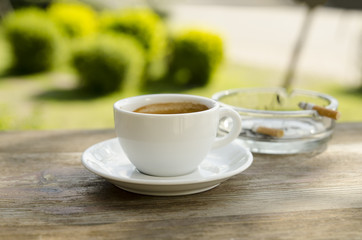 In the cafe,have a cup of coffee, cigarette ashtray and cigarette placed on a wooden table.