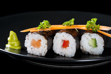 Fresh rolls with salmon, cucumber and pepper on a plate, served with carrot slices and parsley, black background