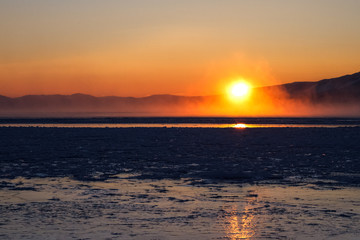 Fototapeta premium Sun just over surface of freezing lake in mist from vaporization, just before sunset 