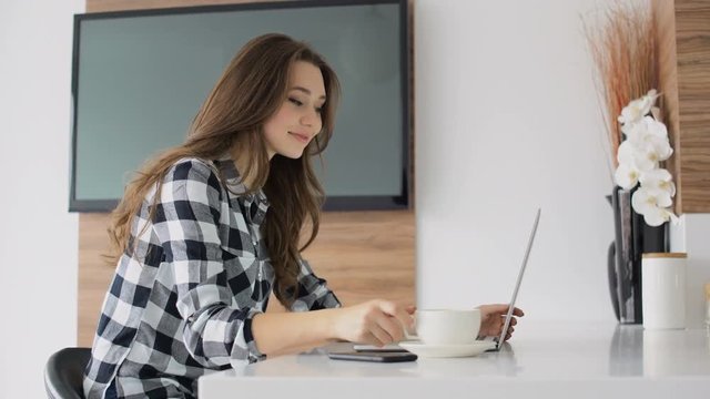 Young lovely woman drinking coffee while using laptop at home 
