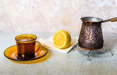 A Cup of coffee, a lemon and boiling water on the kitchen table.