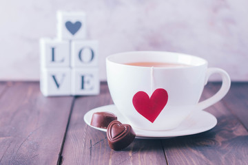 Breakfast on Valentine's day. Cup of tea and two chocolate candies in shape hearts. Message love spelled in wooden blocks. Love or holiday concept. Copy space