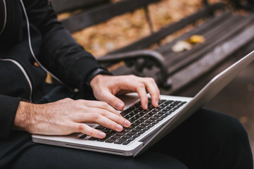 Male hands typing on laptop in the park