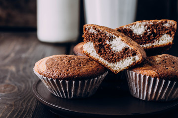 Homemade sweet chocolate vanilla muffins from two types of dough with glass and bottle of milk on wooden table background. Copy space