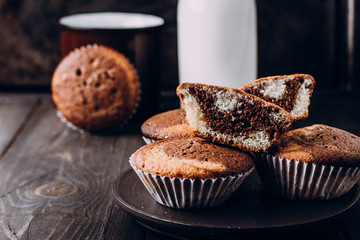 Homemade sweet chocolate vanilla muffins from two types of dough with bottle of milk on wooden table background. Copy space