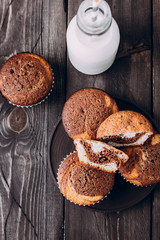 Homemade sweet chocolate vanilla muffins from two types of dough with bottle of milk on wooden table background. Copy space