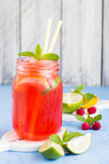 Raspberry lemonade with lemon, lime, mint and ice in the glass on the blue table background. Summer drink
