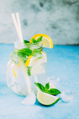 Summer drink, lemonade, mojito cocktail with mint, lemon, lime and ice on blue table background