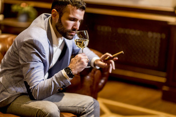 Young man tasting white wine and smoking cigar