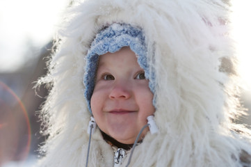 A cute little girl in a fur coat with a hood in the snow. Snowfa - 133803867