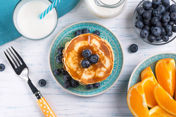 Stack of pancakes with fresh blueberry, honey, milk and orange slices, healthy breakfast concept,...