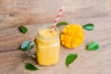 Juicy smoothie from mango in glass mason jar with striped red straw on old wooden background. Healthy life concept, copy space
