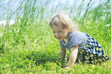 Little girl crawls in the grass by the lake
