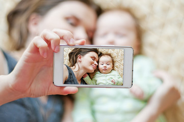 Woman with a baby doing a selfie lying on bed - 133805688
