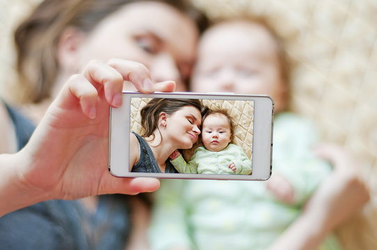Woman with a baby doing a selfie lying on bed