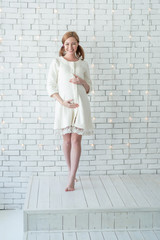Young pregnant girl smiling and standing near white wall