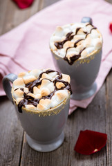 S'mores drink. Two mugs of hot chocolate with marshmallows on a wooden table. Cocoa. Rose petals. Valentine.