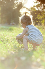 Little girl plays with a ball on the grass in the summer park at