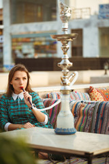 Beautiful young woman smokes a hookah in a cafe