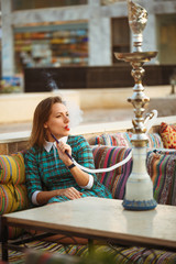 Beautiful young woman smokes a hookah in a cafe