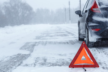 Closeup of red warning triangle with a broken down car in winter