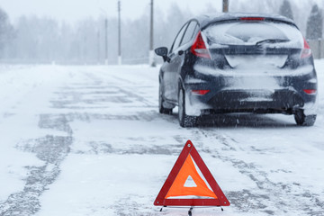 Closeup of red warning triangle with a broken down car in winter