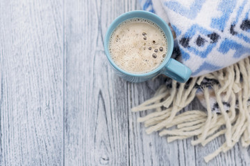 Warm plaid with blue pattern and blue cup of coffee on grey wooden background