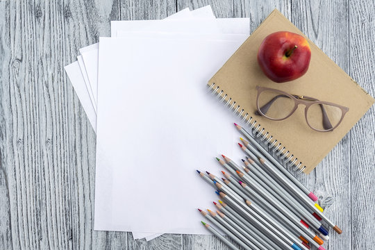 Red apple, glasses, colored pencils and notebook on grey wooden background