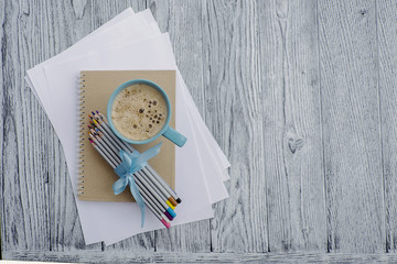 Cup of coffee,  colored pencils, notebook and white sheets of paper on grey wooden background