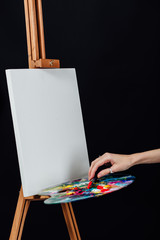 Cute beautiful girl artist painting a picture on canvas an easel. Space for text. Studio black background.