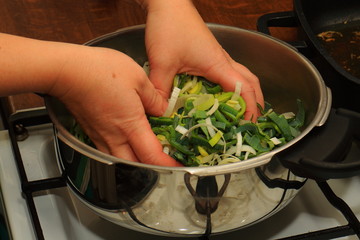 Fresh leeks in a saucepan with hands