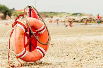 Ring buoy and can of lifeguard on the beach with people in the b