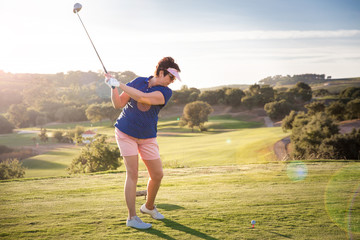 Mature woman playing golf. Golfer hitting golf shot with driver club on course. Beautiful sunny...