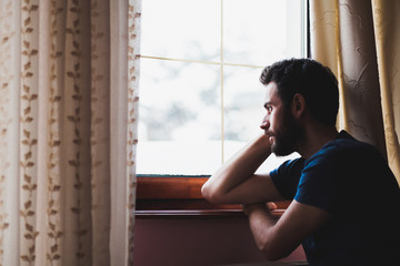 Young sad mad sitting by the window in regret