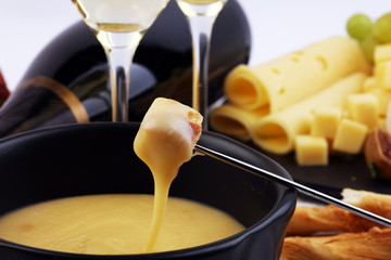 Gourmet Swiss fondue dinner on a winter evening with assorted cheeses on a board alongside a heated...