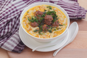 Суп с фрикадельками и лапшой в белой миске на деревянном фоне