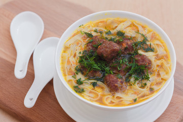 Суп с фрикадельками и лапшой в белой миске на деревянном фоне