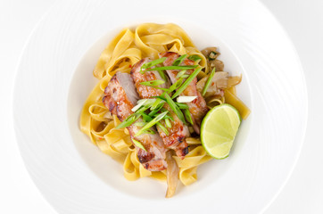 Pasta Fettuccine and caramelized pork with green onions and lime on a plate on a white background, top view