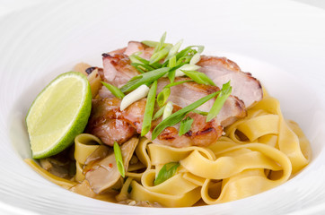 Pasta Fettuccine and caramelized pork with green onions and lime on a plate on a white background, closeup