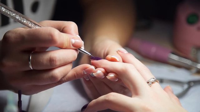 Manicurist paints woman's nails by brush, woman comes to the manicure salon, nail care, business in beauty
