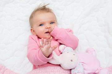 happy infant baby girl smiling on bed with his toy bunny