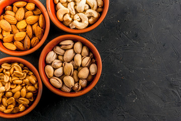 Four bowls with different nuts on a stone kitchen table: cashews, almonds, peanuts and pistachios, copy space, top view